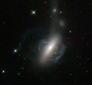 Spiral galaxy with blue-white rings of stars and red-brown streaks of gas. The center glows white so brightly that it seems to form a bar above and below the galaxy.